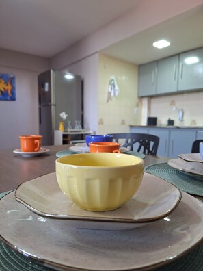 Un coin repas avec une table dressée pour deux personnes, agrémenté d’un bol jaune et de tasses orange.