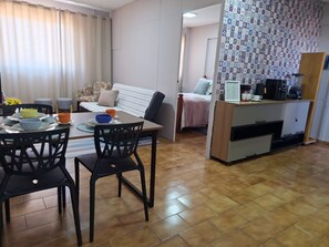 Un espacio habitable compacto con comedor, kitchenette y cama frente a una pared con diseño.