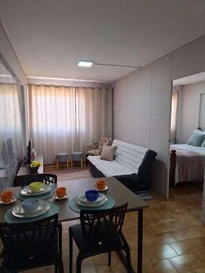 A living room with a sofa, a dining table with chairs, and a kitchen area visible in the background. - New Listing (Rondonópolis)