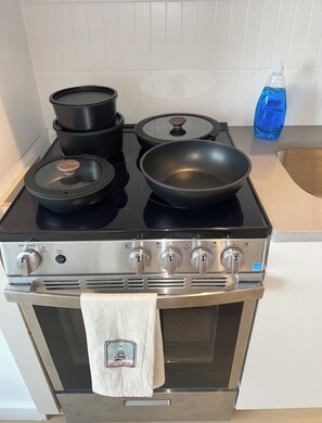 Une cuisine équipée d’une cuisinière, de casseroles, d’une poêle et d’une bouteille de liquide vaisselle.