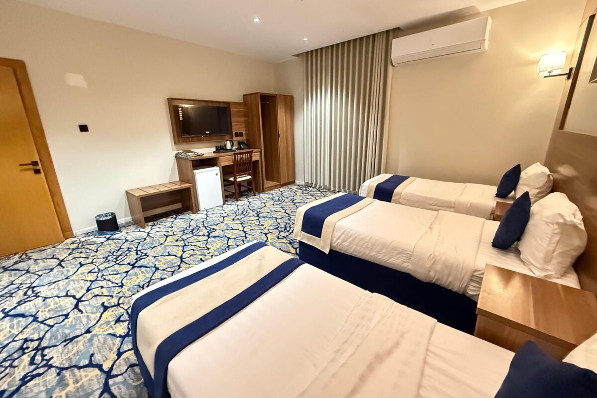 Habitación de hotel con dos camas, un escritorio, una silla, un televisor y un aire acondicionado.