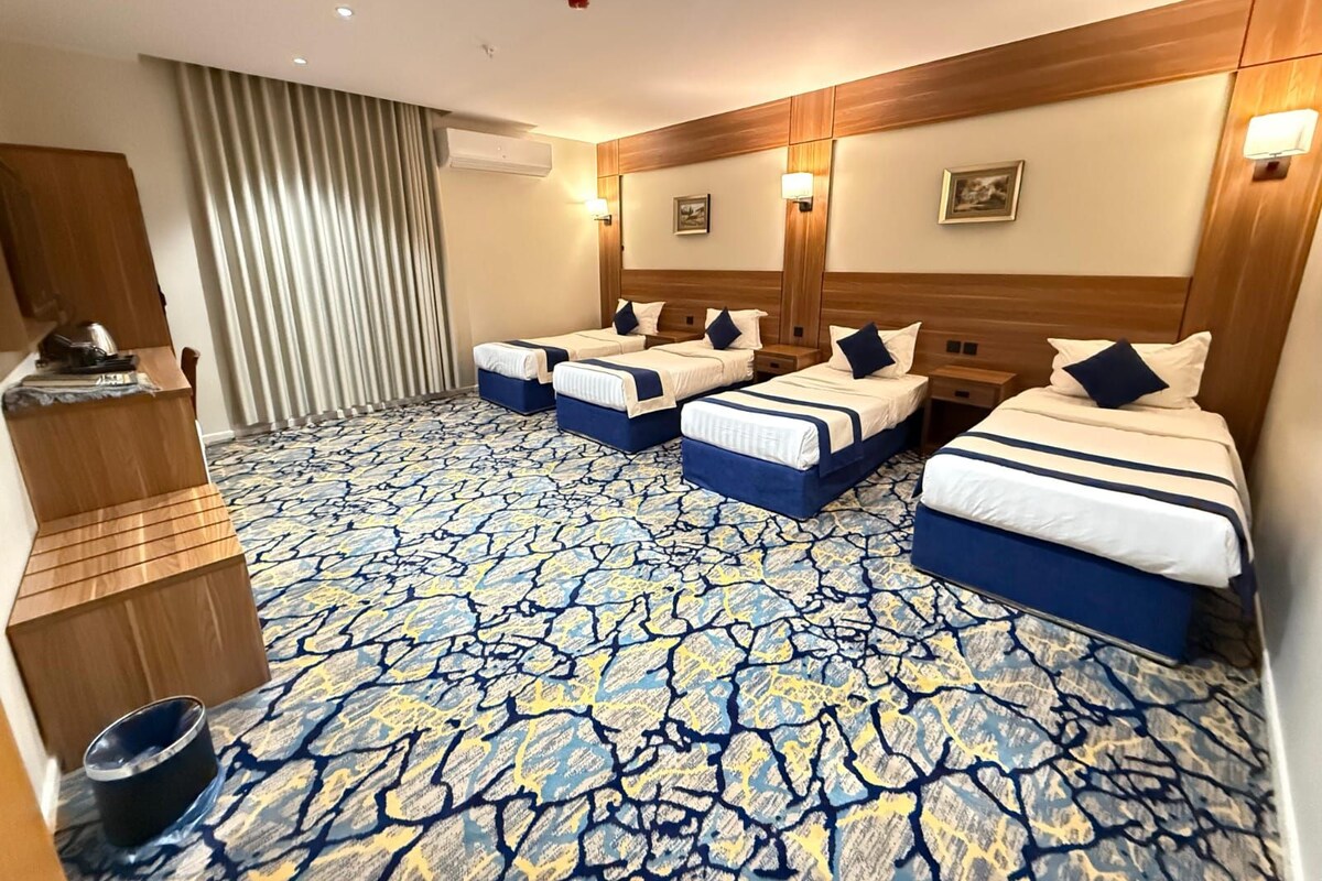 Una habitación de hotel con cuatro camas, un minibar, un armario de madera y una alfombra estampada.