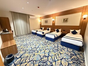 Una habitación de hotel con cuatro camas, un minibar, un armario de madera y una alfombra estampada.