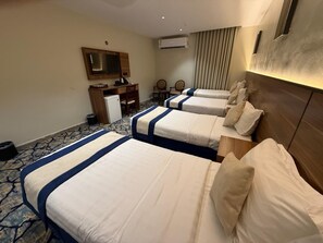 Habitación de hotel con cuatro camas, un escritorio, sillas y un equipo de aire acondicionado.