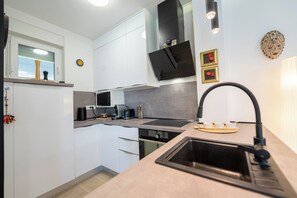 A modern kitchen with white cabinets, a black range hood, a built-in oven, and a stainless steel sink. - Apartment Simba with Private Heated Pool & Jacuzzi (Novalja)