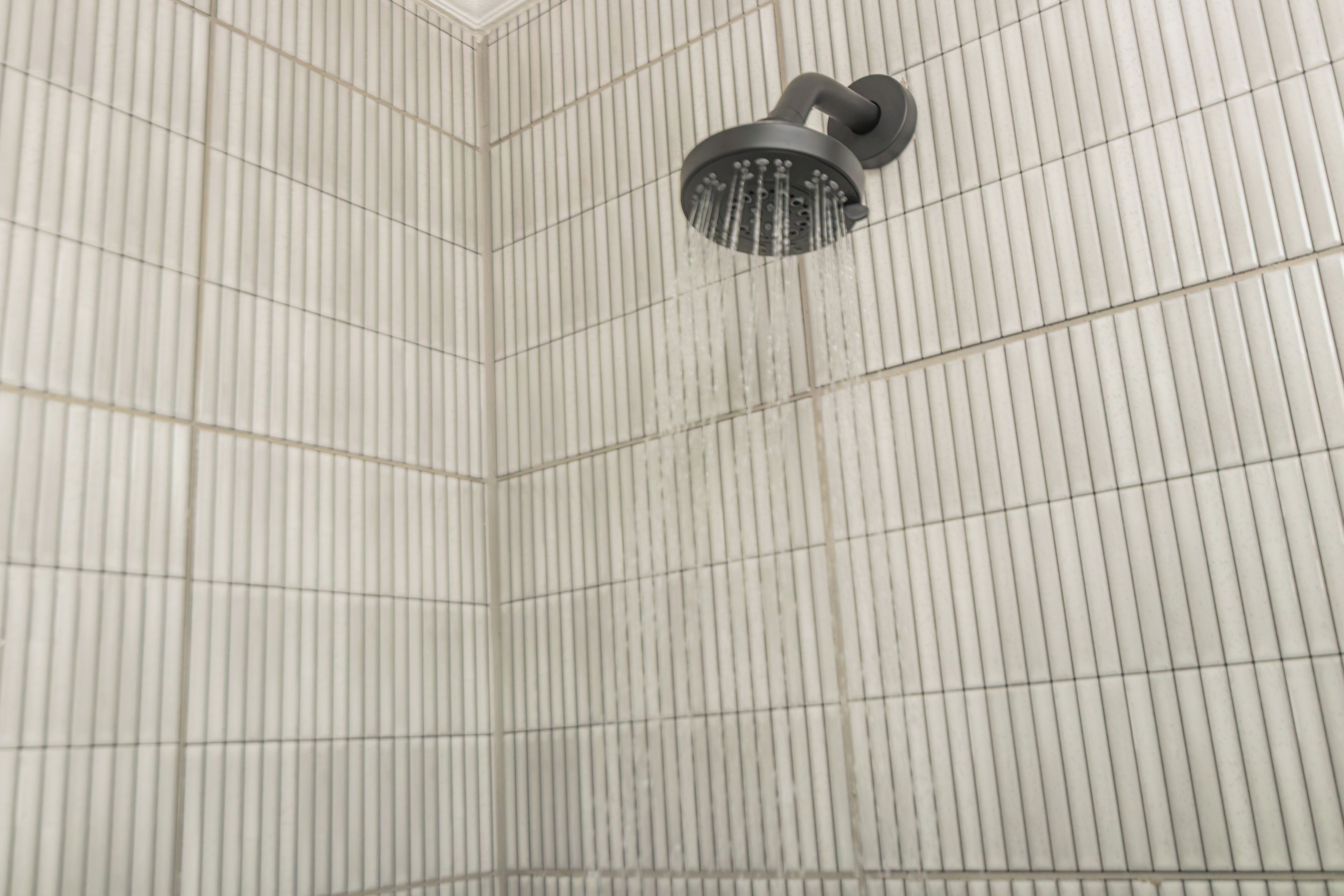 A shower with a curved head and a wall with vertical lines.