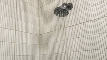 A shower with a curved head and a wall with vertical lines.