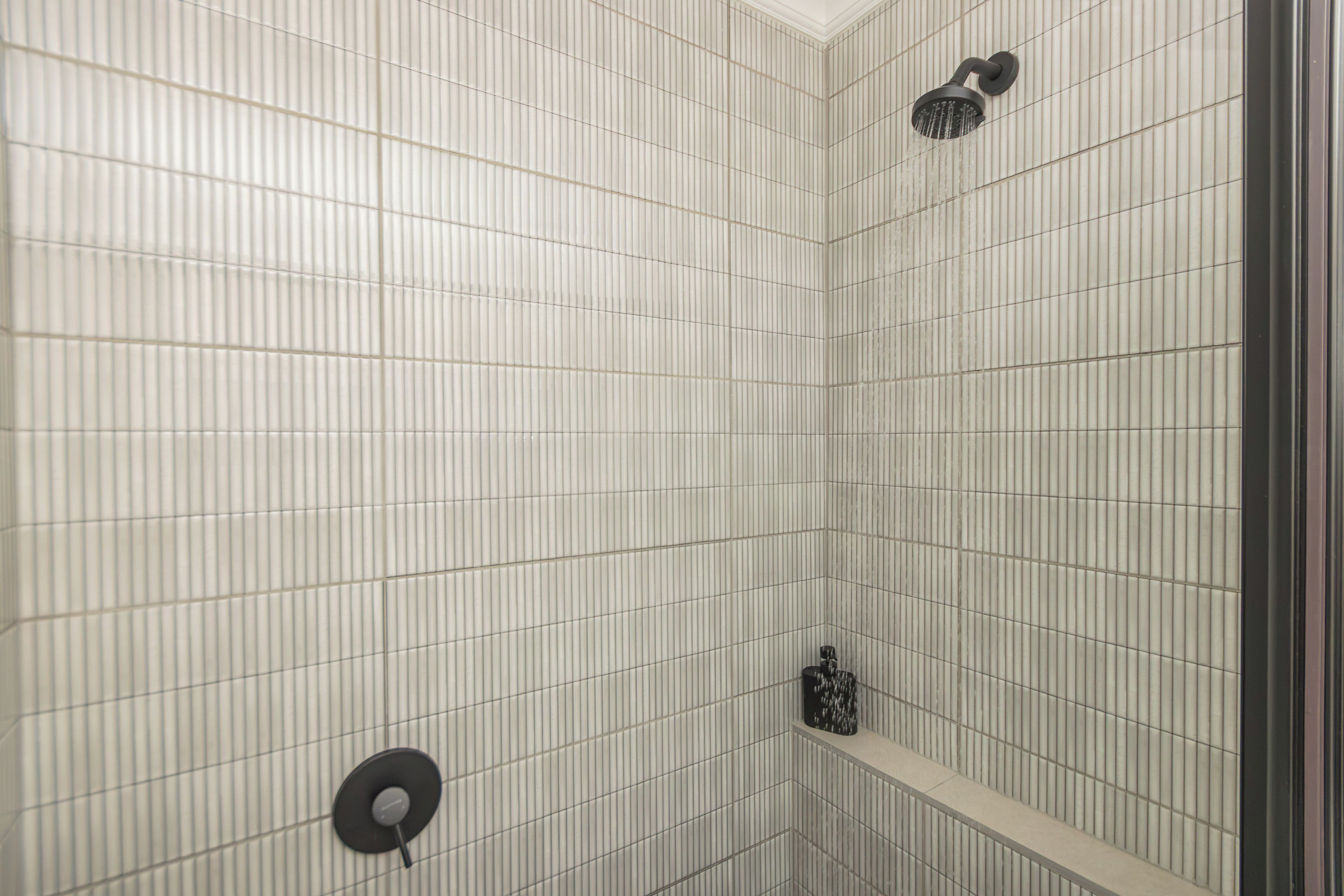 A shower area with a tiled wall, a handheld showerhead, and a fixed overhead showerhead.