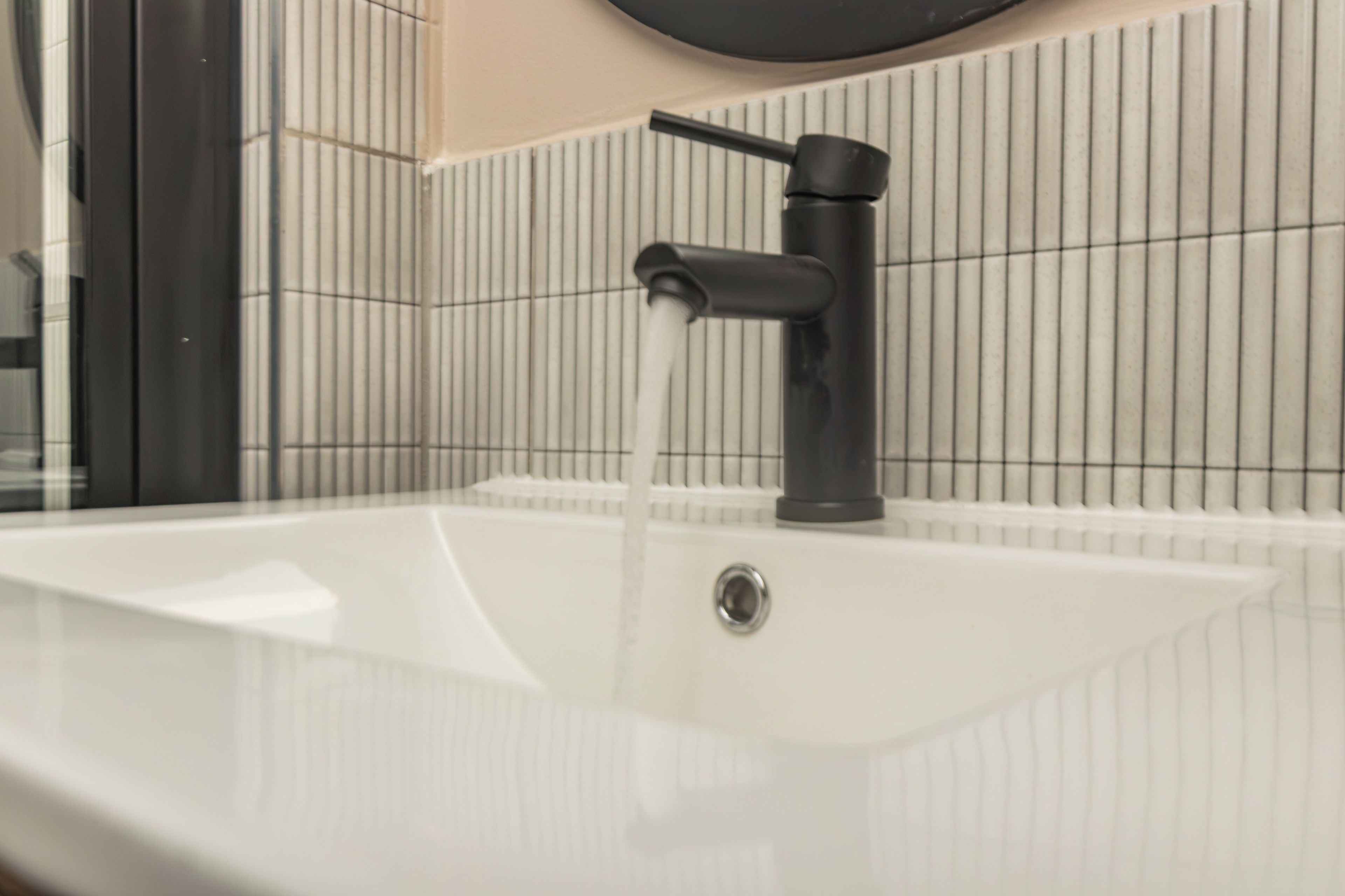 A bathroom with a white sink, a black faucet, and a tiled wall.