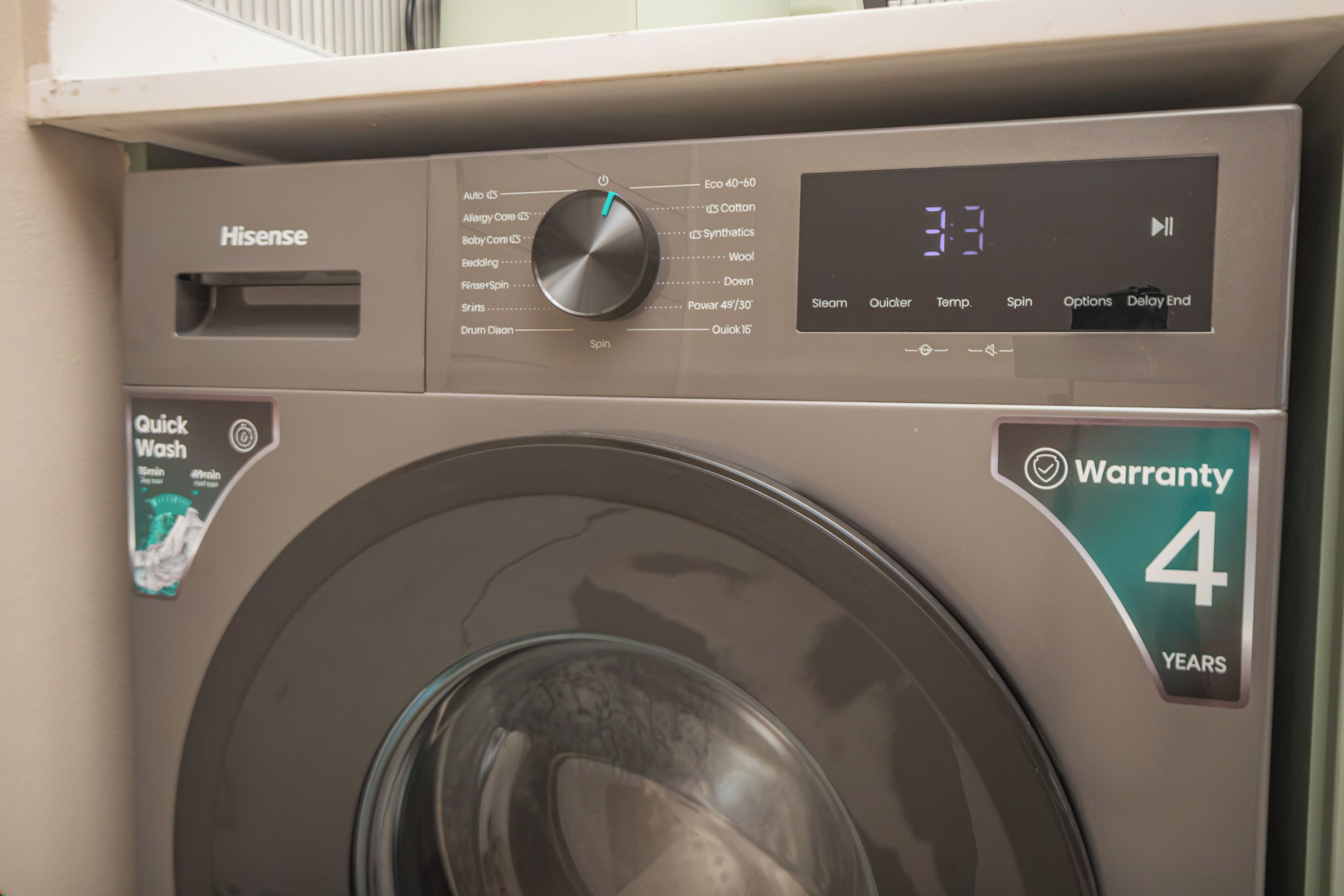 A front view of a Hisense washing machine with a digital display and a warranty sticker.