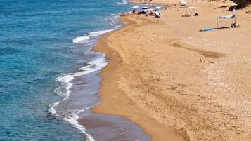 Uma praia com águas cristalinas, uma faixa de areia e montanhas ao fundo.
