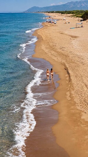 A beach with clear water, a sandy shore, and a mountainous backdrop.