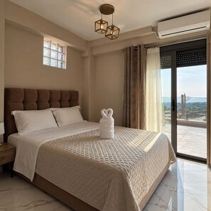 A hotel room with a large bed, a nightstand, a window with curtains, and a view of the outside.