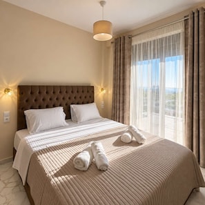 Une chambre d’hôtel avec un grand lit, une tête de lit, deux appliques murales, une fenêtre avec des rideaux et une vue sur l’extérieur.