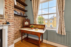 Una habitación con pared de ladrillo, un escritorio de madera con cajones, un radiador y una ventana con cortinas.