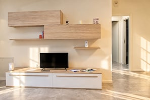 Un salon moderne doté d’un téléviseur à écran plat, d’étagères en bois et d’un meuble de rangement blanc.