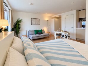Un dormitorio moderno con sofá cama, comedor con mesa y sillas, y kitchenette.