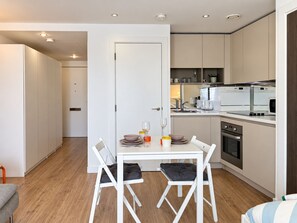 Una cocina moderna con armarios blancos, una mesa de comedor con sillas y un horno empotrado.