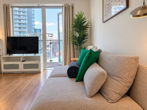 Una sala de estar con un sofá, un televisor de pantalla plana, una planta en maceta y vistas a edificios a través de un ventanal.