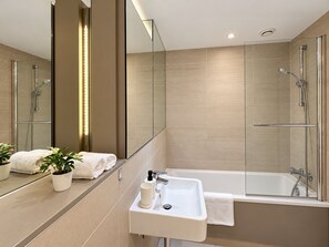 Un baño moderno con ducha envuelta en vidrio, un lavamanos blanco con espejo y una planta en maceta.