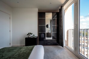 Un dormitorio con cama, cómoda, espejo y vista a la ciudad a través de un amplio ventanal.