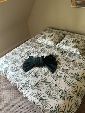Un lit avec une couvre-lit à motifs de feuilles et un coussin vert foncé en forme de nœud.