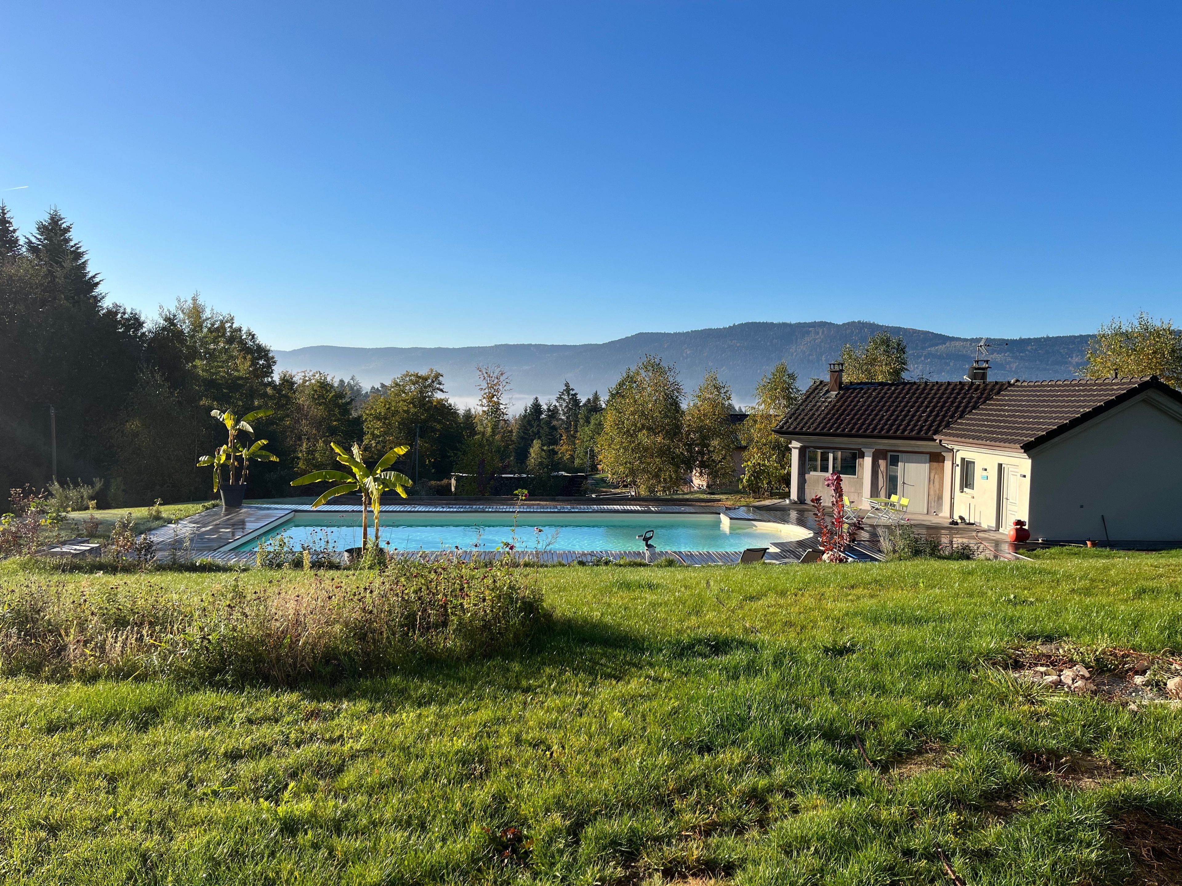 Ein Schwimmbad mit einem Haus im Hintergrund, umgeben von Grünflächen und Bergen.