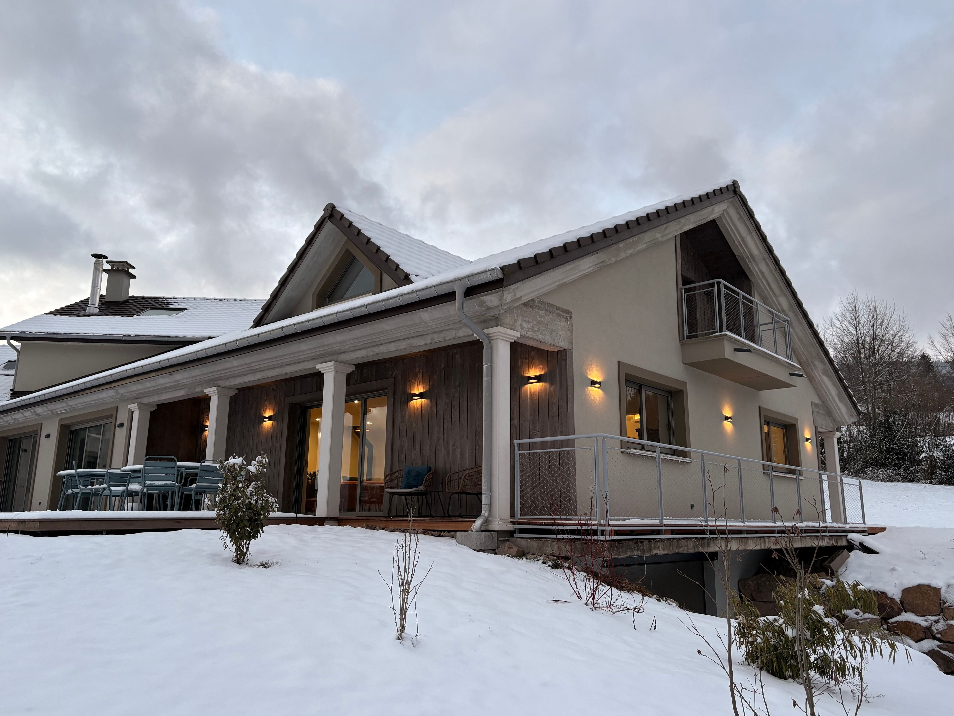 Et toetagers hus med en overdækket veranda, en balkon og et sneklædt landskab.