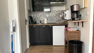 Ett kompakt kök med svarta skåp, ett vitt kylskåp, en kaffebryggare och en papperskorg.