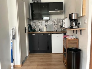 Ett kompakt kök med svarta skåp, ett vitt kylskåp, en kaffebryggare och en papperskorg.
