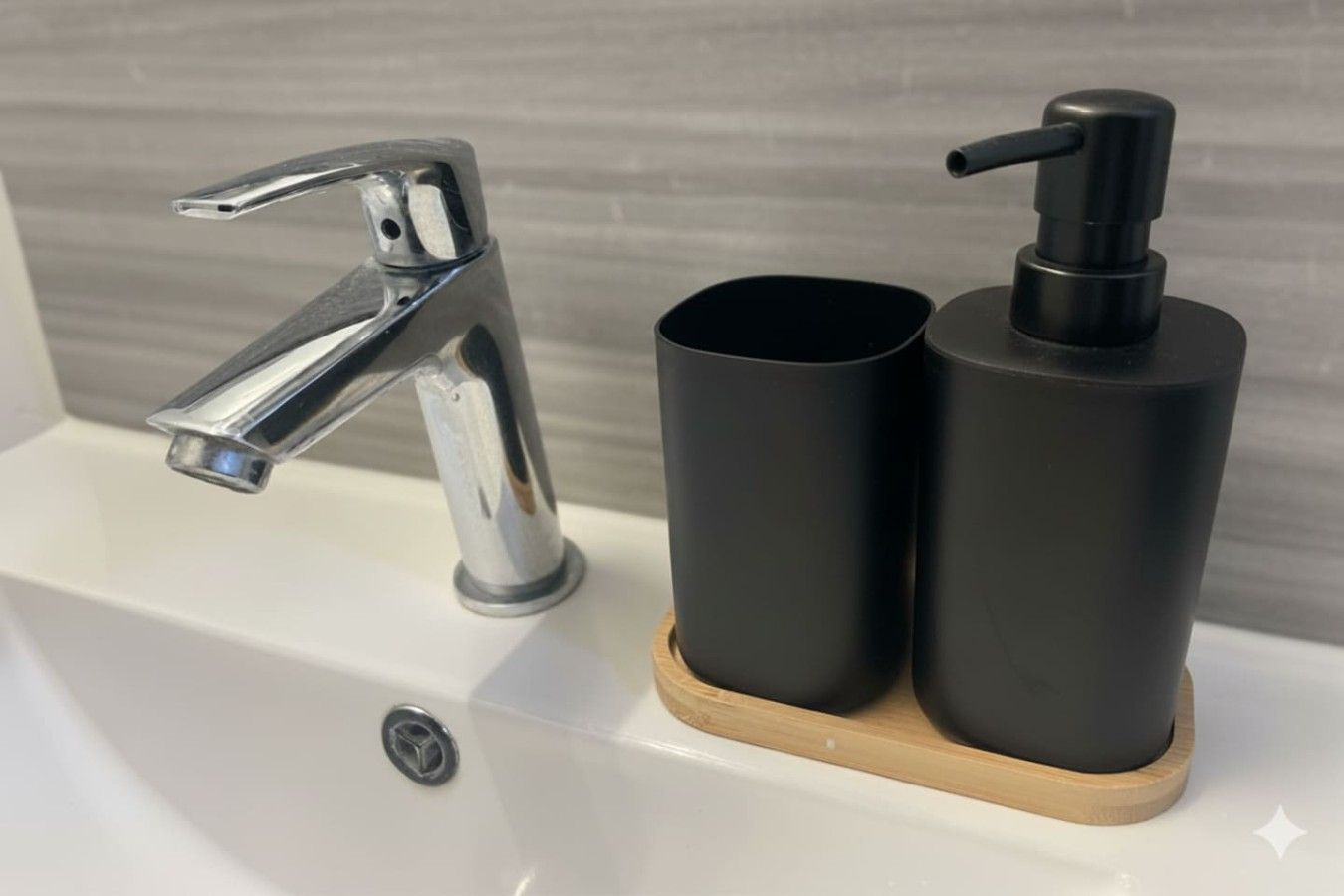 Ein Waschbecken mit chromfarbenem Wasserhahn und zwei schwarzen, zylindrischen Behältern auf einer Holzwasserwaage.