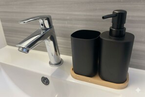 Ein Waschbecken mit chromfarbenem Wasserhahn und zwei schwarzen, zylindrischen Behältern auf einer Holzwasserwaage.