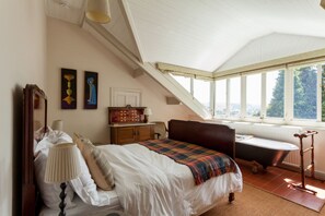 Een slaapkamer met een bed, een dressoir, een kaptafel en een raam met uitzicht op groen.