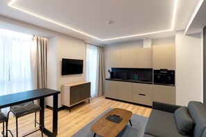 Ein modernes Wohnzimmer mit einer Couch, einem Couchtisch, einem Fernseher und einer Küchenzeile mit Herd und Schränken.