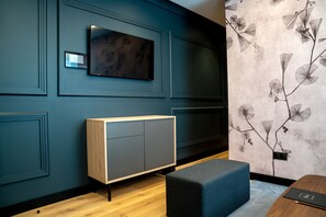 A modern room with a flat-screen TV mounted on a dark blue wall, a wooden cabinet with a grey door, and a wall with a floral pattern. - Genteel Home Mauro Suites VIII (Leon)