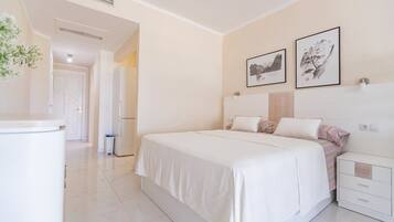 Quarto de hotel com cama, mesas de cabeceira, guarda-roupa e uma porta que dá para outro cômodo.