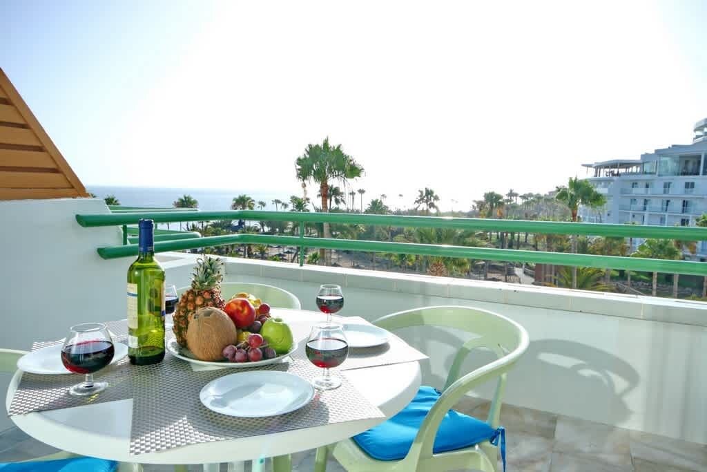 Ein Balkon mit Tisch für zwei Personen, ausgestattet mit einer Weinflasche, einer Obstschale und zwei Weingläsern.