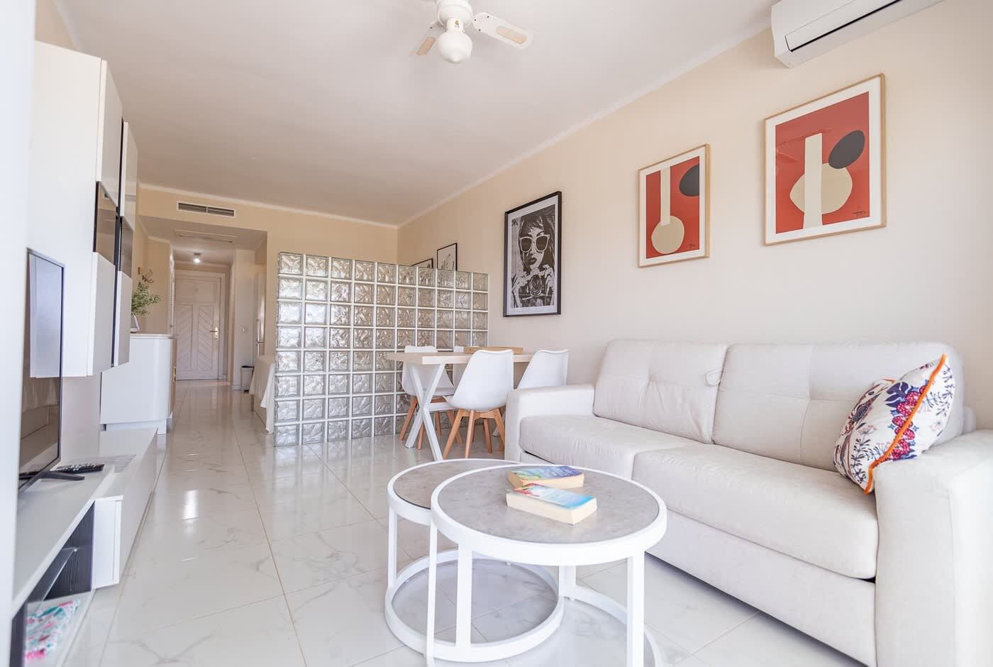 Uma sala de estar moderna com um sofá branco, uma mesa de centro e um espaço de refeições com cadeiras.