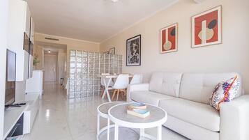 Uma sala de estar moderna com um sofá branco, uma mesa de centro e um espaço de refeições com cadeiras.