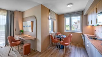 A modern kitchen with a dining area, a flat-screen TV mounted on the wall, and a view of the outdoors.