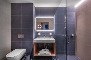 Et moderne badeværelse med en glasafskærmet brusekabine, en hvid vask med et spejl over, og et toilet.