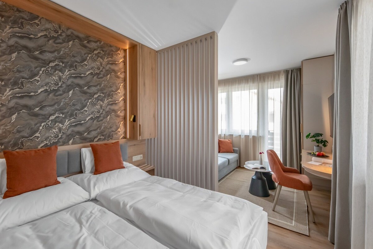 Et hotelværelse med seng, skrivebord, stol og udsigt til det fri.
