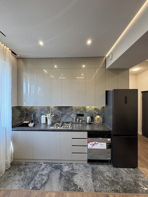 Una cocina moderna con armarios grises, un refrigerador negro y un salpicadero de mármol.