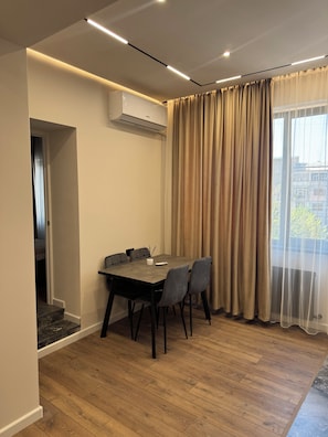 A modern dining area with a table and chairs, an air conditioning unit, and a view through sheer curtains. - Modern New Apartment- Metro at your door (Երևան)