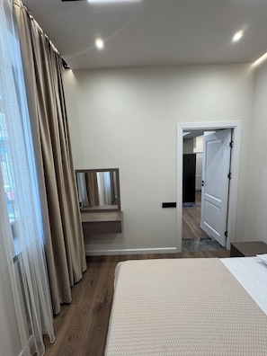 A bedroom with a bed, a mirror, a door leading to a bathroom, and a window with curtains. - Modern New Apartment- Metro at your door (Երևան)
