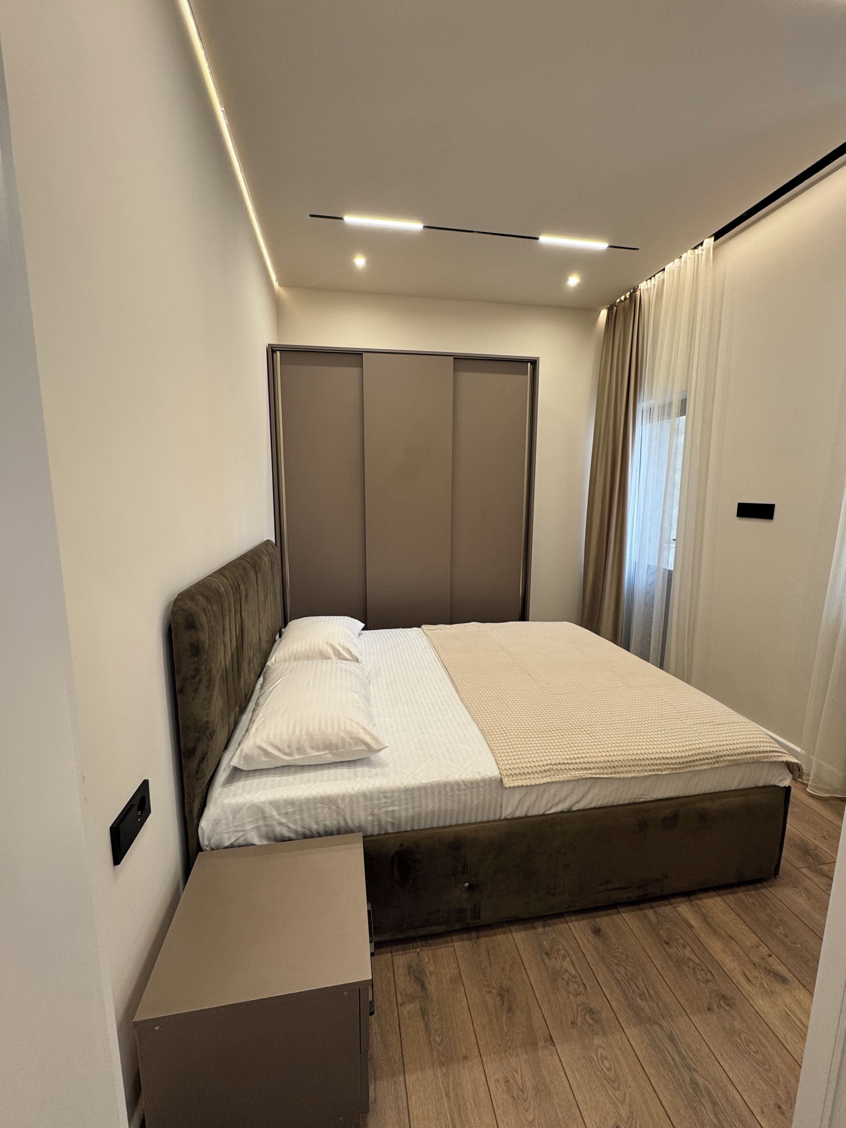 Una camera da letto moderna con pavimento in legno, un letto con biancheria bianca, un comodino e un armadio con ante scorrevoli.