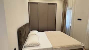 Una camera da letto moderna con pavimento in legno, un letto con biancheria bianca, un comodino e un armadio con ante scorrevoli.