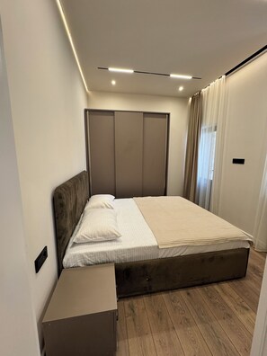 Un dormitorio moderno con piso de madera, una cama con ropa de cama blanca, una mesita de noche y un armario con puertas correderas.