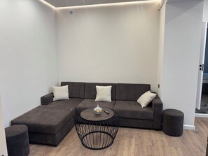 Una sala moderna con un sofá modular, una mesa de centro redonda y dos otomanas.
