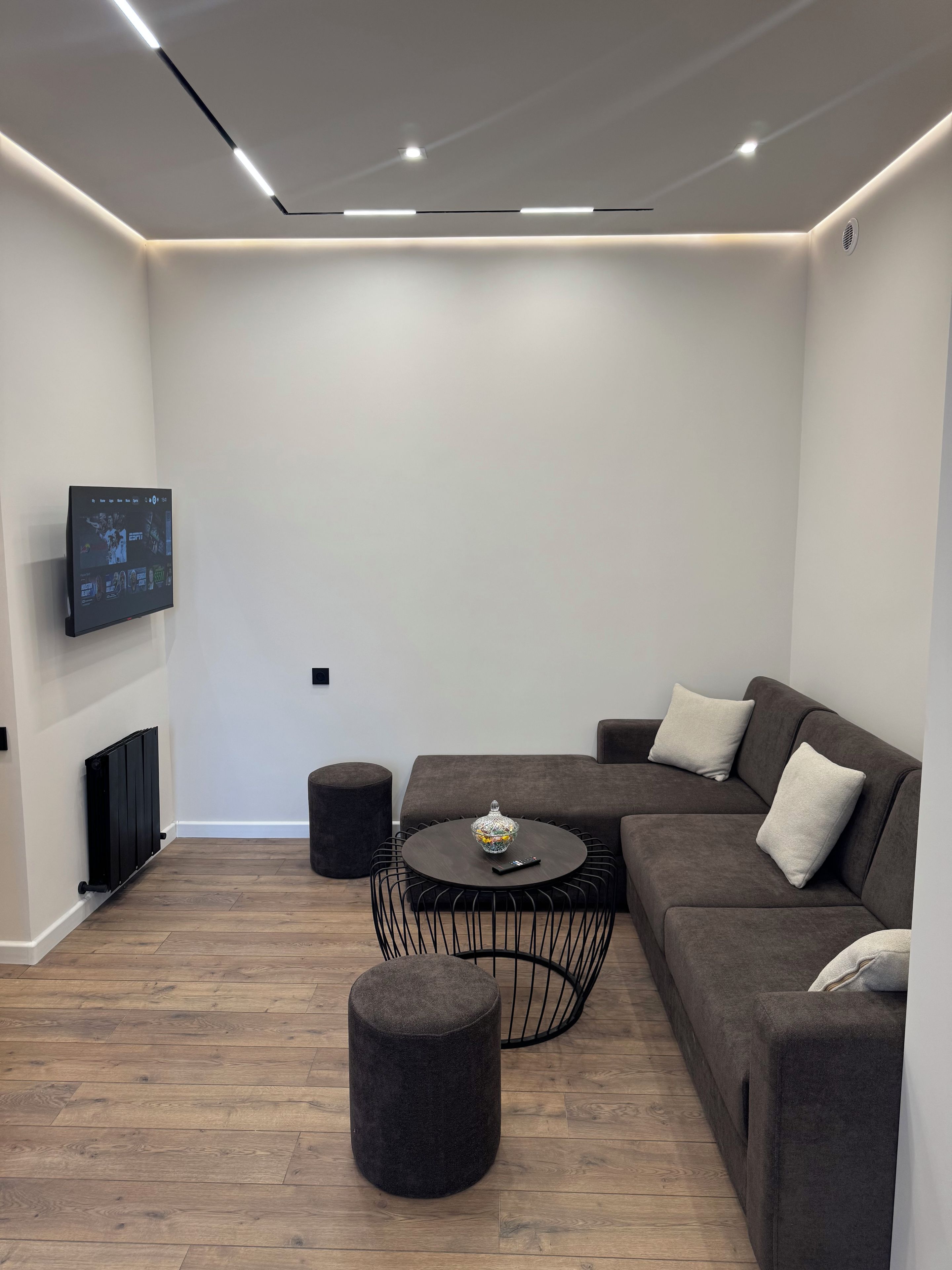 A modern living room with a sectional sofa, a round coffee table, and a flat-screen TV mounted on the wall.